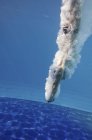 Male diver swimming with splashes underwater after athletic jump in pool. — Stock Photo