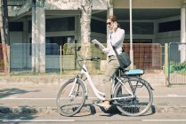 E-bike commuter stopping on street and calling with mobile phone. — Stock Photo