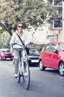 Mujer joven usando bicicleta eléctrica en la calle urbana con coches . - foto de stock