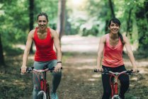 Cheerful female friends riding bikes together in park. — Stock Photo