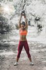 Standing female athlete exercising with kettlebell in park. — Stock Photo