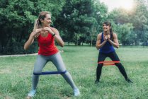 Amis féminins faisant de l'exercice avec des bandes élastiques dans un parc vert
. — Photo de stock
