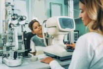 Ophthalmologist using auto refractometer eye examination equipment on boy in clinic. — Stock Photo