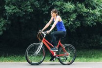 Mujer sonriendo mientras monta en bicicleta en el parque . - foto de stock