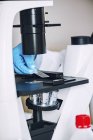 Mão do cientista que pesquisa a amostra na corrediça do microscópio sob o microscópio claro . — Fotografia de Stock