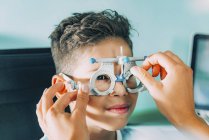 Офтальмолог допомагає хлопчикові носити окуляри під час огляду очей у клініці . — стокове фото