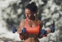 Female athlete exercising with dumbbells outdoors. — Stock Photo