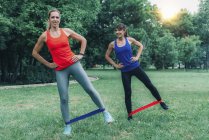 Amis féminins faisant de l'exercice avec des bandes élastiques dans un parc vert . — Photo de stock