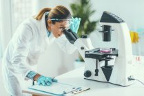 Cientista feminina pesquisando amostra em placa de Petri sob microscópio de luz
. — Fotografia de Stock