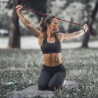 Athletische Frau dehnt sich nach dem Sport im Park mit Gummiband. — Stockfoto