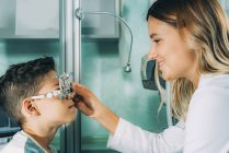 Oftalmologista ajudando menino vestindo óculos enquanto exame ocular na clínica . — Fotografia de Stock