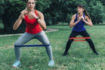 Amis féminins faisant de l'exercice avec des bandes élastiques dans un parc vert
. — Photo de stock