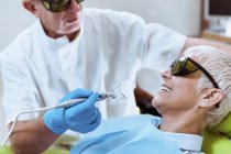 Dentiste homme effectuant le blanchiment des dents au laser chez la patiente à la clinique dentaire . — Photo de stock