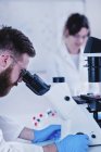 Young male researcher looking at sample under microscope in laboratory. — Stock Photo