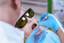 Dentista masculino realizando clareamento dos dentes a laser em paciente do sexo feminino na clínica odontológica . — Fotografia de Stock