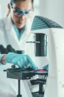 Cientista feminina pesquisando amostra em placa de Petri sob microscópio de luz . — Fotografia de Stock