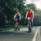 Two women riding bicycles together on park road. — Stock Photo