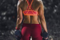 Vista posteriore dell'atleta donna che si allena con i manubri nel parco . — Foto stock