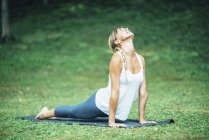 Frau macht Yoga, praktiziert Bhujangasana-Kobra-Position auf Matte im Park. — Stockfoto