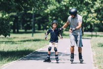 Grandfather teaching grandson rollerskating in summer park. — Stock Photo