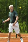 Jogador sênior ativo praticando tênis na quadra . — Fotografia de Stock