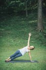 Mulher fazendo ioga, praticando prancha lateral posar vasisthasana no tapete no parque . — Fotografia de Stock