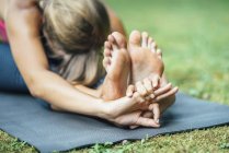 Young woman doing yoga, practicing seated forward bend paschimottanasana on mat in park. — Stock Photo