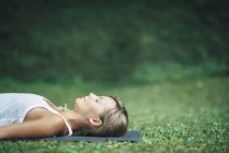Frau macht Yoga und meditiert in Shavasana-Leichenstellung auf Matte im Park. — Stockfoto