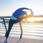 Female jogger stretching after training outdoors during sunset. — Stock Photo