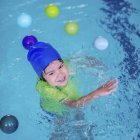 Малыш в синей кепке учится плавать в бассейне . — стоковое фото