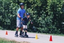 Profesor sénior de patinaje sobre ruedas con niño practicando en clase en el parque . - foto de stock