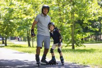 Grandfather and grandson in helmets rollerskating in park. — Stock Photo