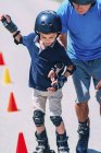 Junge lernt Rollschuhlaufen mit Opa auf Straße mit Kegeln. — Stockfoto