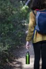 Vista posteriore della donna che cammina sul sentiero forestale con in mano una bottiglia d'acqua . — Foto stock