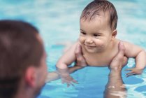 Smiling baby boy in swimming pool water in male hands. — Stock Photo