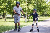 Grandfather and grandson in helmets rollerskating in park. — Stock Photo