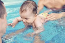 Cute baby boy swimming with instructor and mother in pool water. — Stock Photo