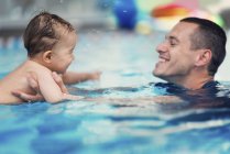 Instructor con lindo bebé en la clase de natación en la piscina pública . - foto de stock