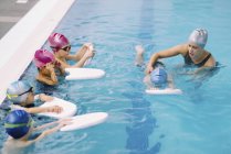 Instructor de natación trabajando con un niño mientras los niños observan en la piscina . - foto de stock