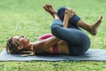 Junge Frau macht Yoga, übt Liegeposition auf Matte im Park. — Stockfoto