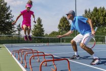 Teenie-Mädchen im Tennistraining auf dem Platz mit männlichem Trainer. — Stockfoto