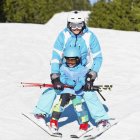 Маленький хлопчик в зимовому одязі вчиться кататися на лижах з батьком на засніженому курорті . — стокове фото