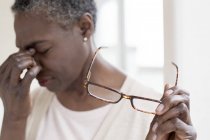 Mature woman with tension headache holding glasses. — Stock Photo