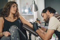 Татуювальник зосереджена на тату роботи на жіночому клієнті. — стокове фото