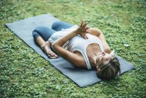 Yoga donna meditando con le ginocchia piegate e le mani in posizione di preghiera sul tappeto nel parco . — Foto stock
