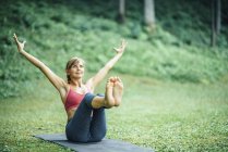 Young woman doing yoga and practicing navasana boat pose on mat in park. — Stock Photo