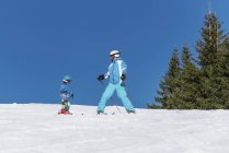 Menino em roupas de inverno aprendendo esqui com o pai no resort nevado . — Fotografia de Stock