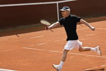 Jogador de tênis sênior ativo correndo com raquete na quadra . — Fotografia de Stock