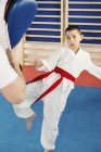 Coup de pied garçon en classe de taekwondo avec entraîneur . — Photo de stock