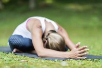 Woman doing yoga and practicing seated forward bend on mat in park. — Stock Photo